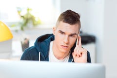 Sammanträde för ung man vid datoren och användamobiltelefonen royaltyfri foto Sammanträde för ung man vid datoren och användamobiltelefonen royaltyfri foto