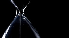 The sand flow in the hourglass with black background and lateral light backlight in lateral composition in loop