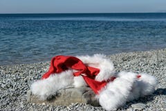 Santa Claus clothing and hat lies on a large stone on the seashore. Santa went swimming stock photos Santa Claus clothing and hat lies on a large stone on the seashore. Santa went swimming stock photos