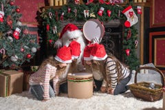 Santa Claus et enfants ouvrant des présents à la cheminée image stock Santa Claus et enfants ouvrant des présents à la cheminée image stock