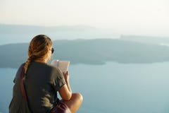 Santorini, Греция, 21-ое сентября 2018, турист ослабляет читающ книгу в заходе солнца стоковое изображение rf Santorini, Греция, 21-ое сентября 2018, турист ослабляет читающ книгу в заходе солнца стоковое изображение rf