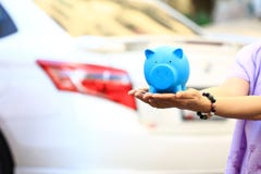 Saving money and loans for car concept, Young woman holding blue piggy with standing at the car parking lot background, Auto royalty free stock photo Saving money and loans for car concept, Young woman holding blue piggy with standing at the car parking lot background, Auto royalty free stock photo