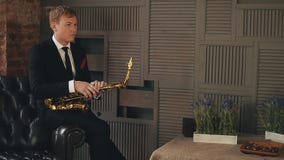 Saxophonist στη συνεδρίαση σακακιών γευμάτων στην καρέκλα με το χρυσό saxophone Καλλιτέχνης της Jazz φιλμ μικρού μήκους Saxophonist στη συνεδρίαση σακακιών γευμάτων στην καρέκλα με το χρυσό saxophone Καλλιτέχνης της Jazz φιλμ μικρού μήκους
