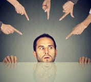 Scared man employee hiding under the table being accused by many people who point fingers at him Royalty Free Stock Photos Scared man employee hiding under the table being accused by many people who point fingers at him Royalty Free Stock Photos