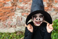 Scary Little Girl In A Witch Costume Smiles Against A Brick Wall. Happy Halloween Royalty Free Stock Photos