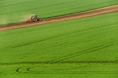 Scenic View Of Modern Farming Tractor Which Plowing Green Field. Agriculture Tractor Cultivating Wheat Field And Creating Green Ab Stock Images Scenic View Of Modern Farming Tractor Which Plowing Green Field. Agriculture Tractor Cultivating Wheat Field And Creating Green Ab Stock Images