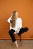Sch?nes Modell auf dem orange Hintergrund, der auf dem Stuhl im wei?en Hemd und in der schwarzen Hose sitzt stockbilder Sch?nes Modell auf dem orange Hintergrund, der auf dem Stuhl im wei?en Hemd und in der schwarzen Hose sitzt stockbilder