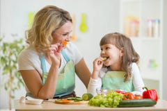 Scherzi la ragazza e la madre che mangiano le verdure sane dell'alimento fotografia stock Scherzi la ragazza e la madre che mangiano le verdure sane dell'alimento fotografia stock