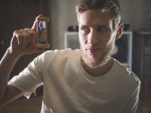 Schließen Sie herauf Porträt des jungen bärtigen Mannes in der zufälligen netten Haltezeit-Sandsanduhr zu Hause stockbild Schließen Sie herauf Porträt des jungen bärtigen Mannes in der zufälligen netten Haltezeit-Sandsanduhr zu Hause stockbild