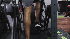 Schließen Sie oben von den Beinen des schwarzen Mannes auf elliptischem Trainer stock video footage Schließen Sie oben von den Beinen des schwarzen Mannes auf elliptischem Trainer stock video footage