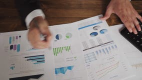 Schließen Sie oben von den Händen eines Geschäftsmannes mit dem Stift, der am Schreibtisch arbeitet und Diagramme und Diagramme a stock footage Schließen Sie oben von den Händen eines Geschäftsmannes mit dem Stift, der am Schreibtisch arbeitet und Diagramme und Diagramme a stock footage