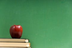 School books and chalkboard. School books and apple in front of school chalkboard, blank add your own text copy space School books and chalkboard. School books and apple in front of school chalkboard, blank add your own text copy space
