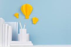 School template - white books, stationery, decorative paper yellow lightbulbs origami on white desk and soft blue background.