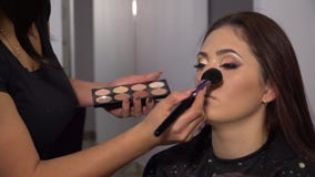 Schoonheidszaal Het jonge mooie meisjesmodel zit als voorzitter De make-upkunstenaar maakt meisjesmake-up Brunette in een schoonh stock video Schoonheidszaal Het jonge mooie meisjesmodel zit als voorzitter De make-upkunstenaar maakt meisjesmake-up Brunette in een schoonh stock video