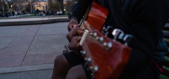 Schwarzer Kerl, der eine Gitarre spielt und glückliches Sitzen in einer Bank eines Parks singt lizenzfreie stockfotografie Schwarzer Kerl, der eine Gitarre spielt und glückliches Sitzen in einer Bank eines Parks singt lizenzfreie stockfotografie