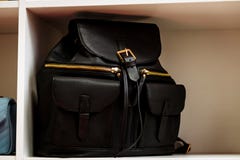 Schwarzer lederner Rucksack mit goldenen Rei?verschlusstaschen auf einem wei?en Regal im Speicher lizenzfreies stockfoto Schwarzer lederner Rucksack mit goldenen Rei?verschlusstaschen auf einem wei?en Regal im Speicher lizenzfreies stockfoto