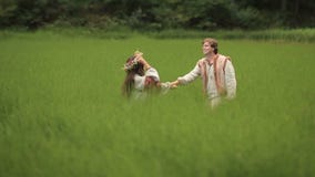 Schöne Paare in der Liebe im traditionellen ukrainischen Kleidungsgehen und Händchenhalten am grünen Feld stock video footage Schöne Paare in der Liebe im traditionellen ukrainischen Kleidungsgehen und Händchenhalten am grünen Feld stock video footage