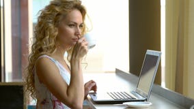 Schönes blondes Mädchen im Kleid unter Verwendung des Laptops im Café Junge Frau trinkt Kaffee und das Arbeiten an Notizbuch stock footage Schönes blondes Mädchen im Kleid unter Verwendung des Laptops im Café Junge Frau trinkt Kaffee und das Arbeiten an Notizbuch stock footage