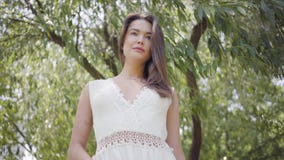 Schönes junges Mädchen des Porträts mit dem langen brunette Haar, das eine lange weiße Sommermode-Kleiderstellung unter trägt stock video footage Schönes junges Mädchen des Porträts mit dem langen brunette Haar, das eine lange weiße Sommermode-Kleiderstellung unter trägt stock video footage