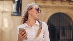Schönes junges tragendes weißes Hemd der Geschäftsfrau und mit Smartphone beim Gehen in das Internet des Stadtzentrum-Sommers stock video footage Schönes junges tragendes weißes Hemd der Geschäftsfrau und mit Smartphone beim Gehen in das Internet des Stadtzentrum-Sommers stock video footage