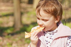 Schönes kleines Mädchen, das draußen ein köstliches Lebensmittel der Pizza genießt, lizenzfreies stockbild Schönes kleines Mädchen, das draußen ein köstliches Lebensmittel der Pizza genießt, lizenzfreies stockbild