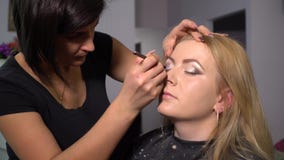 Schönheits-Saal Junges schönes Mädchenmodell sitzt im Stuhl Maskenbildner macht Mädchenmake-up Maskenbildner stock footage Schönheits-Saal Junges schönes Mädchenmodell sitzt im Stuhl Maskenbildner macht Mädchenmake-up Maskenbildner stock footage