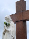 Scène dans un cimetière : statue de Vierge Marie tenant un bouquet des fleurs blanches devant une grande croix de granit image libre de droits Scène dans un cimetière : statue de Vierge Marie tenant un bouquet des fleurs blanches devant une grande croix de granit image libre de droits