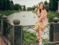 se repose sur une barrière, dans les mains d'un chapeau, d'une robe beige en fleur et d'un chandail beige Belle fille red-haired photo stock se repose sur une barrière, dans les mains d'un chapeau, d'une robe beige en fleur et d'un chandail beige Belle fille red-haired photo stock