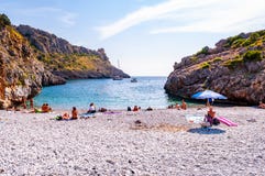 Sea yachts floating, people resting on amazing Cala Bianca beach surrounded by rocks of Tyrrhenian sea bay with crystal clear