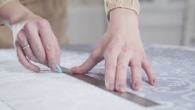 Seamstress measures length of the the fabric with chalk and a ruler