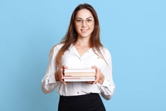 Secrétaire énergique mince de sourire tenant la pile de livres des deux mains, ayant satisfait l'expression du visage, lookin dir photo libre de droits Secrétaire énergique mince de sourire tenant la pile de livres des deux mains, ayant satisfait l'expression du visage, lookin dir photo libre de droits