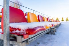 Sedili variopinti vuoti dello stadio di calcio di calcio nell'inverno coperto in neve - Sunny Winter Day con chiaro cielo blu in immagine stock libera da diritti Sedili variopinti vuoti dello stadio di calcio di calcio nell'inverno coperto in neve - Sunny Winter Day con chiaro cielo blu in immagine stock libera da diritti