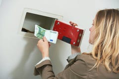Seguridad del dinero La mujer puso efectivo de los ahorros en la caja fuerte de la pared fotografía de archivo libre de regalías Seguridad del dinero La mujer puso efectivo de los ahorros en la caja fuerte de la pared fotografía de archivo libre de regalías