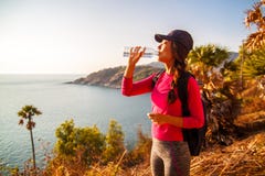 Seitenansicht der Frau mit Rucksack und einer Flasche Wasser Meer beim Sitzen betrachtend auf Hügel gegen Himmel lizenzfreies stockbild Seitenansicht der Frau mit Rucksack und einer Flasche Wasser Meer beim Sitzen betrachtend auf Hügel gegen Himmel lizenzfreies stockbild