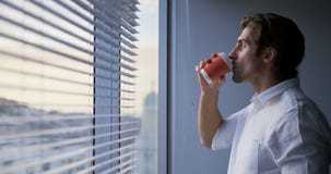 Seitenansicht des trinkenden Kaffees der jungen kaukasischen männlichen Exekutive nahe Fenster im modernen Büro 4k stock video footage Seitenansicht des trinkenden Kaffees der jungen kaukasischen männlichen Exekutive nahe Fenster im modernen Büro 4k stock video footage
