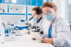 selectieve nadruk van wetenschappers in medische maskers en beschermende brillen die door microscopen op regenten kijken stock foto selectieve nadruk van wetenschappers in medische maskers en beschermende brillen die door microscopen op regenten kijken stock foto