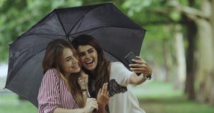 Selfie Time For Two Ladies On Rain Day Taking Pictures Using A Phone , Under The Umbrella.4k Royalty Free Stock Photo Selfie Time For Two Ladies On Rain Day Taking Pictures Using A Phone , Under The Umbrella.4k Royalty Free Stock Photo