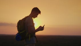 Sempre e dappertutto in tocco Un viaggiatore con uno zaino utilizza uno smartphone Siluetta sul fondo di tramonto archivi video Sempre e dappertutto in tocco Un viaggiatore con uno zaino utilizza uno smartphone Siluetta sul fondo di tramonto archivi video