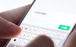 Sending I love you text message with mobile phone. Online dating, texting or catfishing concept. Romance fraud, scam.