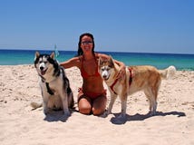 Senhora atrativa na praia ensolarada com areia branca e os céus azuis, com os dois cães eyed azuis bonitos fotografia de stock royalty free Senhora atrativa na praia ensolarada com areia branca e os céus azuis, com os dois cães eyed azuis bonitos fotografia de stock royalty free