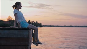 A senhora delgada nova é sentar-se à superfície da àgua no fulgor do por do sol do verão e relaxar video estoque A senhora delgada nova é sentar-se à superfície da àgua no fulgor do por do sol do verão e relaxar video estoque