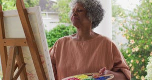 Senior african american woman painting while standing on the porch of the house