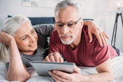 Senior couple with digital tablet resting in bed together Stock Photography Senior couple with digital tablet resting in bed together Stock Photography