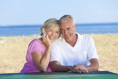 Senior Couple Using Cell Phone at Table By Beach Royalty Free Stock Photo Senior Couple Using Cell Phone at Table By Beach Royalty Free Stock Photo