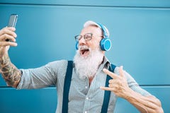 Senior crazy man taking self video while listening music with headphones - Hipster guy having fun using mobile smartphone