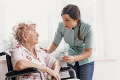 Senior on wheelchair, supporting nurse giving her glass of water stock photos Senior on wheelchair, supporting nurse giving her glass of water stock photos