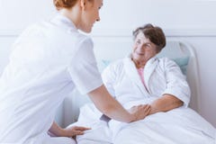 Senior grey woman lying in white hospital bed with young helpful nurse holding her hand royalty free stock photography Senior grey woman lying in white hospital bed with young helpful nurse holding her hand royalty free stock photography