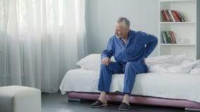 Senior male suffering sharp back pain, sick person getting up from bed, morning