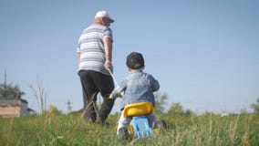 Senior man grandfather teaches his grandson to ride a bike in nature. He pulls it by the rope, the kid learns to ride a