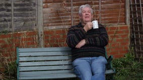 Senior man sitting outside drinking tea or coffee.